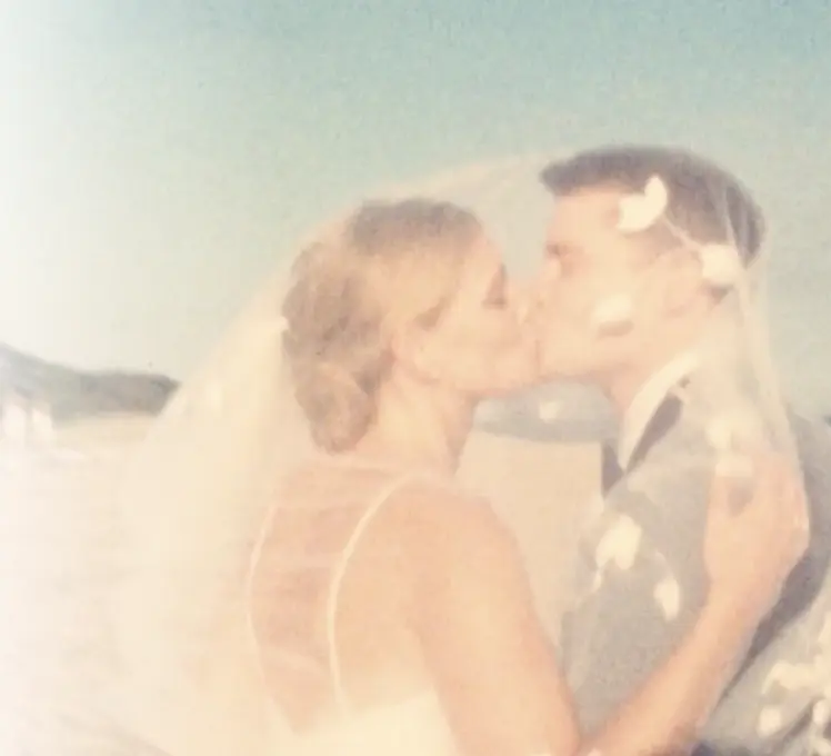 Bride and groom sharing a soft kiss as petals fall